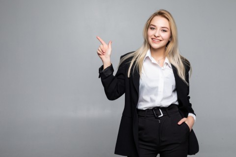 young-business-woman-pointing-finger-to-the-side-on-isolated-grey-wall